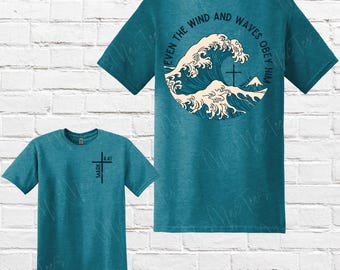 May include: Two teal blue t-shirts with a Christian message. The back of one shirt features a wave design with the text "Even the wind and waves obey him". The front of the other shirt has the text "Mark 4:41" and a cross.