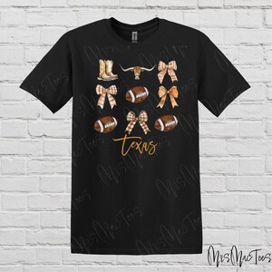 May include: Black t-shirt with a design featuring footballs, bows, cowboy boots, and a longhorn steer. The text "Texas" is printed in orange on the shirt.