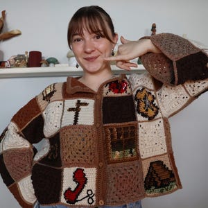 May include: A long-sleeved crochet cardigan constructed from various square patches in shades of brown, tan, and cream. The garment features a button-up front and diverse graphic motifs, including a red telephone, a house, and abstract patterns.