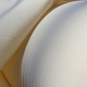 May include: Close-up of a white fabric with a smooth texture. The fabric is folded in half, creating a soft, rounded shape.