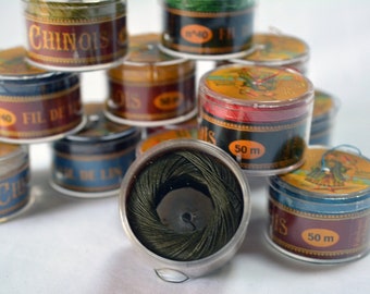 May include: A collection of spools of thread in various colors, including green, red, blue, and black. The spools are labeled with the text "Fil de Lin" and "50 m".