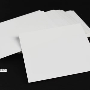 May include: A stack of white blank cards on a black background. The cards are rectangular and have a smooth surface.