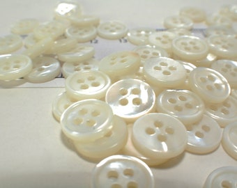 May include: A pile of white pearl buttons with four holes each. The buttons are smooth and shiny.