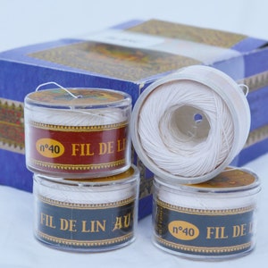 May include: Four spools of white linen thread in clear plastic containers with gold and red labels. The labels read "n°40 FIL DE LIN AU".