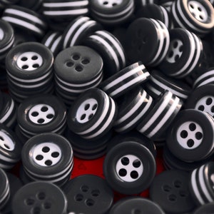 May include: A pile of black and white striped buttons. The buttons have four holes each and are arranged in a random pattern.