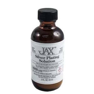 May include: A brown glass bottle with a black cap labelled "JAX Silver Plating Solution". The bottle contains a liquid solution for silver plating. The label includes warnings about eye irritation and instructions to keep out of reach of children. The bottle contains 2 fluid ounces (59 ml) of solution.