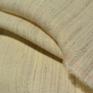 Puede incluir: Primer plano de una tela beige con un sutil patrón tejido. La tela tiene una textura ligeramente rugosa y una sensación suave y natural.