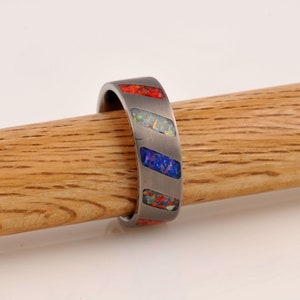 May include: A silver ring with a diagonal pattern of red, blue, and white opal inlay.