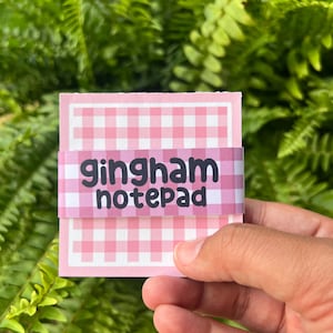May include: A pink and white gingham notepad with the text "gingham notepad" printed on the front.