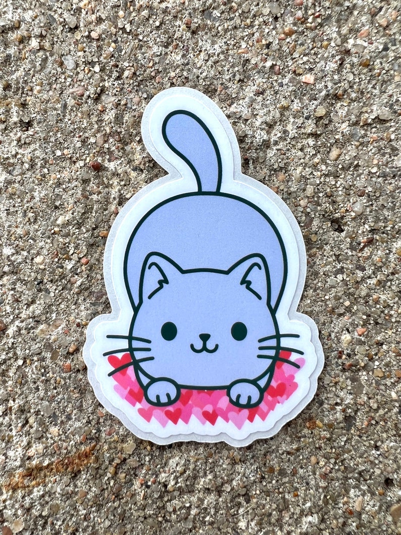 May include: A purple cat sticker with a white outline, sitting on a bed of pink hearts. The cat has black eyes and a small, pink nose.