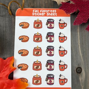 May include: A sticker sheet with fall-themed illustrations. The sheet features images of pumpkin pie, candles, jars of apple butter, and pumpkin spice lattes. The text "Fall Favorites Sticker Sheet" is at the top of the sheet, and the text "crafted by taryn" is at the bottom.