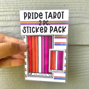 May include: A sticker pack featuring two pride flag themed tarot cards. The larger card is labeled "The Lesbian" and features a lesbian pride flag. The smaller card is also labeled "The Lesbian" and features a smaller version of the lesbian pride flag.