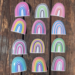May include: Twelve individual stickers shaped like semi-circular rainbows, each featuring a unique combination of four distinct colored stripes. The designs include various color palettes such as pink, blue, green, yellow, and black, all set against a white background.