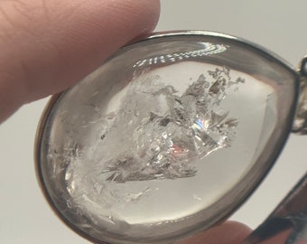 May include: A clear teardrop-shaped pendant with a silver setting. The pendant contains a cluster of clear crystals.