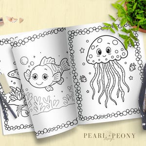 Puede incluir: Libro para colorear abierto con dos p&aacute;ginas con dibujos lineales de un pez y una medusa. El libro est&aacute; rodeado de l&aacute;pices, una goma de borrar, un sacapuntas y un estuche. El libro est&aacute; sobre una superficie de madera clara.