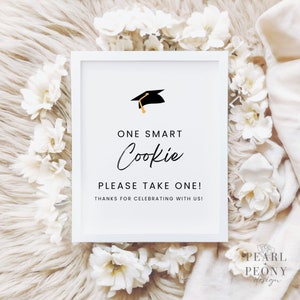 May include: White sign with a black graduation cap icon and the text "ONE SMART Cookie PLEASE TAKE ONE! THANKS FOR CELEBRATING WITH US!"