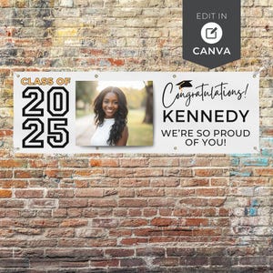 May include: A white banner with the text "CLASS OF 2025" and a photo of a smiling woman. The banner also reads "Congratulations! KENNEDY WE'RE SO PROUD OF YOU!" in black script. The banner is hanging on a brick wall.