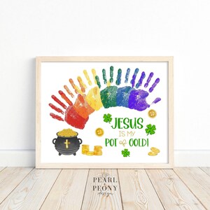 Könnte beinhalten: Ein Regenbogen-Handabdruck-Kunstdruck mit dem Text "Jesus ist mein Topf Gold!" und einem Topf Gold mit einem Kreuz.