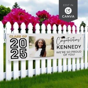May include: A white banner with the text "CLASS OF 2025" and "Congratulations! KENNEDY WE'RE SO PROUD OF YOU!" is displayed on a white picket fence. A photo of a smiling woman is in the center. Pink flowers are above the fence.
