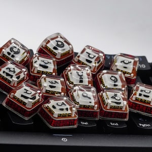 May include: A collection of red and white keycaps with black symbols and a clear plastic top. The keycaps are arranged on a black keyboard.