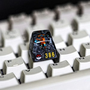 May include: A black and blue keyboard keycap with a colorful graphic of a character from a popular video game. The keycap has the number 386 printed on it.