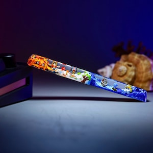 May include: A clear, rectangular, glass-like object with a colorful image of cartoon characters and a ship on a blue ocean. The image is encased in the object, giving it a 3D effect.