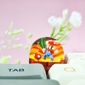 May include: A clear glass dome with a miniature figurine of a video game character inside. The character is wearing a red hat and blue overalls. The dome is sitting on a keyboard with the keys "TAB" and "Q" visible.