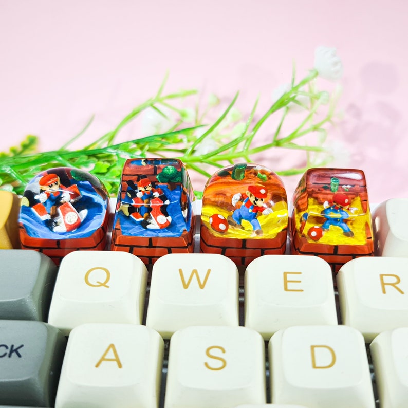 May include: Four colorful keycaps featuring characters from the Super Mario Bros. video game series. The keycaps are made of clear resin with a brick pattern and are designed to fit standard mechanical keyboards. The keycaps are arranged in a row on a keyboard with the keys QWER and ASD visible.