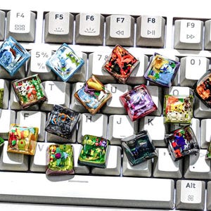May include: A white keyboard with colorful keycaps featuring various designs. The keycaps are made of clear plastic with images printed on them. The keycaps are arranged in a random pattern on the keyboard.