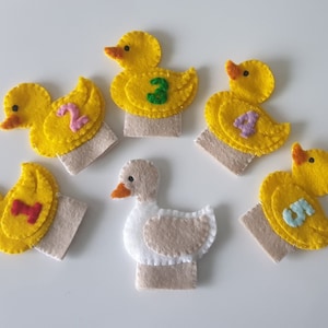 Könnte beinhalten: Fünf gelbe Filz-Fingerpuppen in Form von Enten, jede mit einer anderen Zahl auf der Vorderseite. Die Zahlen sind 1, 2, 3, 4 und 5. Es gibt auch eine weiße Filz-Fingerpuppe in Form einer Gans.