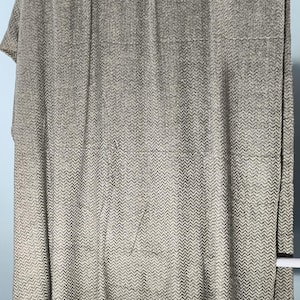 Puede incluir: Una manta o colcha grande, rectangular, con estampado de espiga gris y blanco. La tela está drapeada sobre una barra blanca sobre un fondo azul claro. El patrón es un diseño de chevrón repetido.