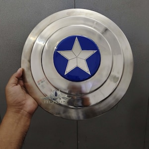 May include: A silver metal shield with a blue and white star in the centre. The shield is round and has a raised edge.