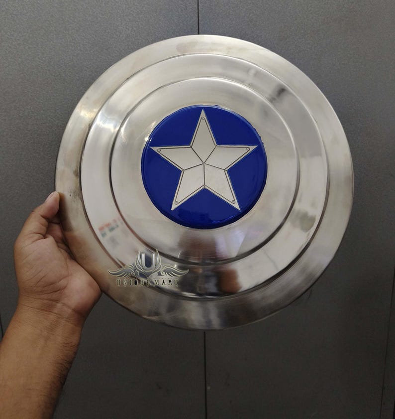 May include: A silver metal shield with a blue and white star in the centre. The shield is round and has a raised edge.