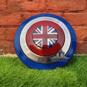 May include: A round, blue and red shield with a silver centre. The shield has a Union Jack flag design in the centre.