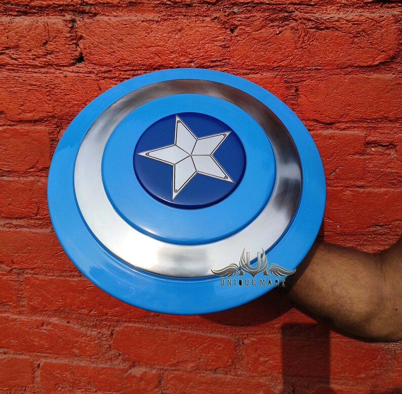 May include: A blue and silver Captain America shield with a white star in the centre. The shield is held in a person's hand.