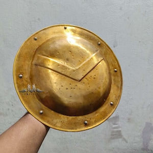 May include: A round, gold-colored metal shield with a raised, pointed design in the center. The shield has a decorative border with small metal studs.
