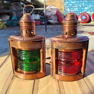 Pu&ograve; includere: Due lampade di segnalazione nautiche antiche in rame con lenti in vetro. La lampada a sinistra ha una lente verde e dice "Dritto" sul lato. La lampada a destra ha una lente rossa e dice "Sinistro" sul lato.