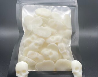 May include: A clear plastic bag filled with white wax melts shaped like skulls and bones. Two white skull-shaped wax melts are outside the bag.
