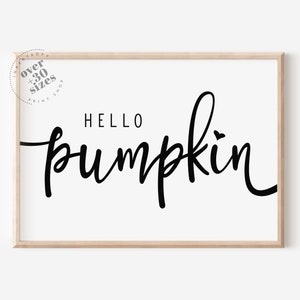 Könnte beinhalten: Gerahmter Druck mit den Worten "HELLO pumpkin" in schwarzer Schrift auf weißem Hintergrund. Der Druck hat einen hellen Holzrahmen und ein kleines Herz über dem "i" in pumpkin. Oben links befindet sich ein rundes Logo mit Text.