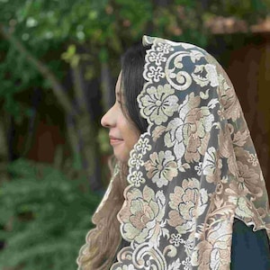 May include: A white lace mantilla with a floral design in beige and gold. The lace is delicate and intricate, with a scalloped edge.