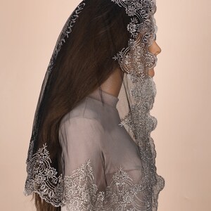 Peut inclure: Une mantille en dentelle noire avec des broderies argent&eacute;es. La dentelle est festonn&eacute;e et pr&eacute;sente un motif floral.