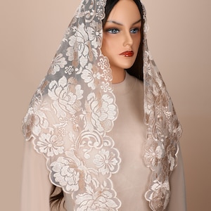 May include: A white lace mantilla with gold embroidery featuring a floral pattern. The mantilla is draped over a mannequin's head and shoulders.