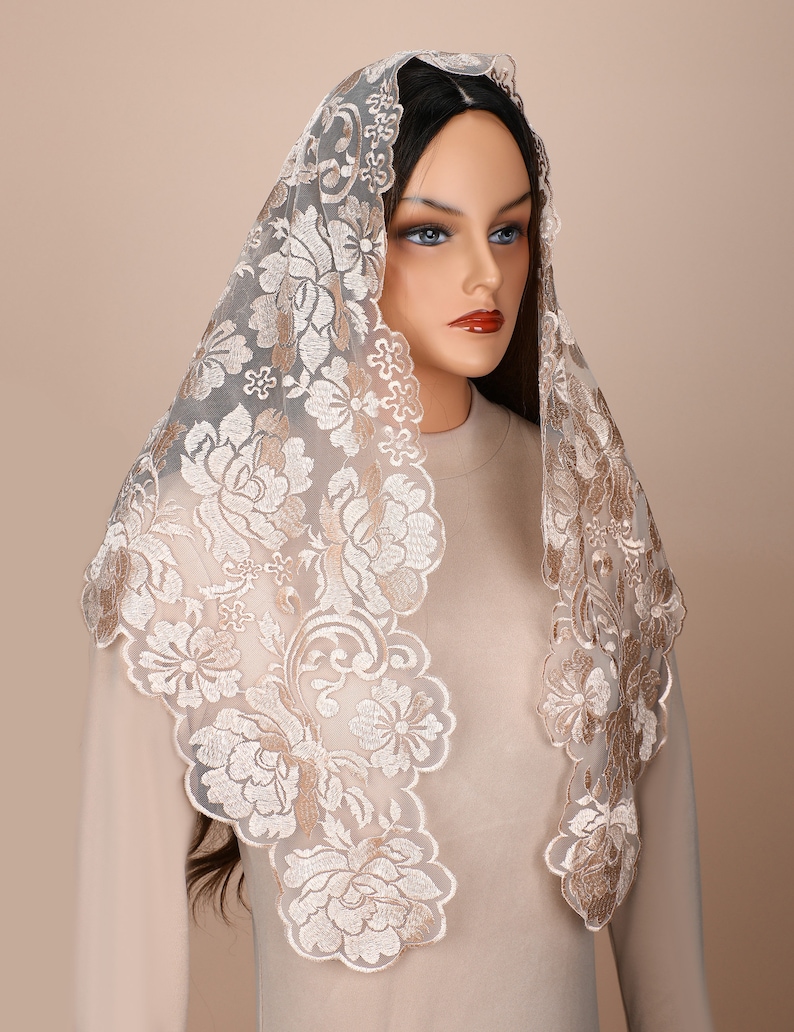 May include: A white lace mantilla with gold embroidery featuring a floral pattern. The mantilla is draped over a mannequin's head and shoulders.