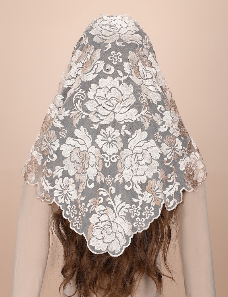 May include: A white lace mantilla with a floral pattern in a beige colour. The lace is delicate and intricate, with a scalloped edge.