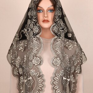 May include: A black and gold embroidered veil with a floral design. The veil is made of sheer fabric and is draped over a mannequin. The gold embroidery creates a decorative border around the edges of the veil.