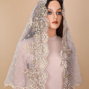May include: A sheer white veil with gold lace trim. The lace features a floral design. The veil is draped over a mannequin's head.