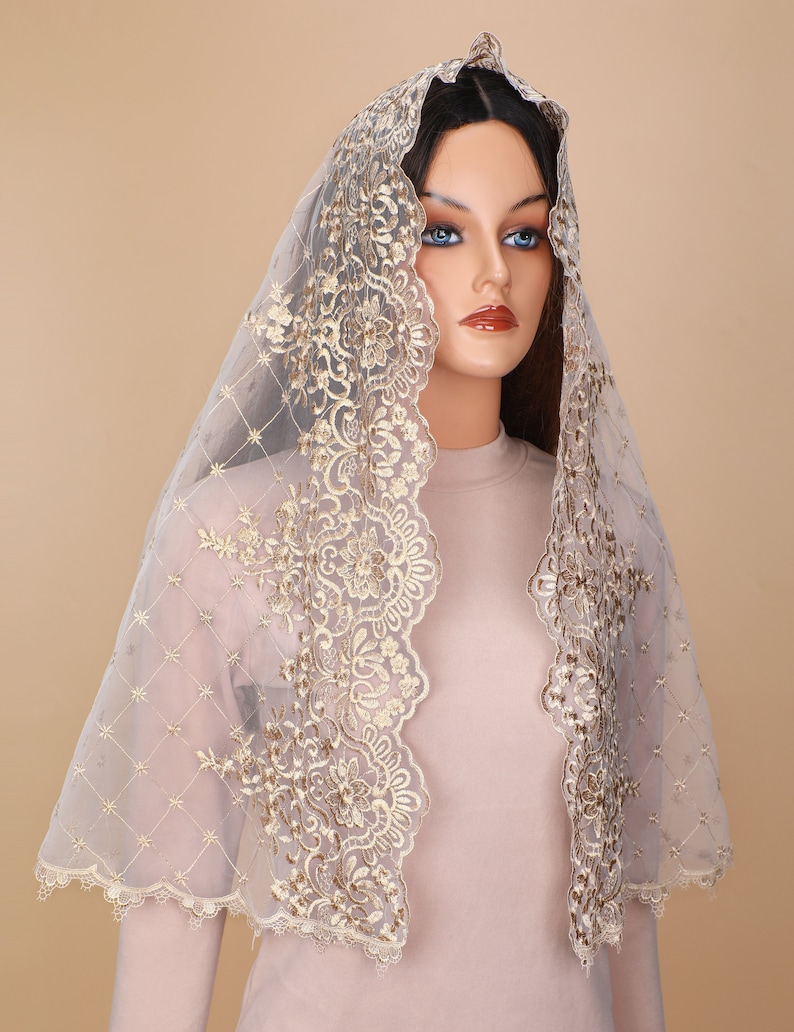 May include: A sheer white veil with gold lace trim. The lace features a floral design. The veil is draped over a mannequin's head.