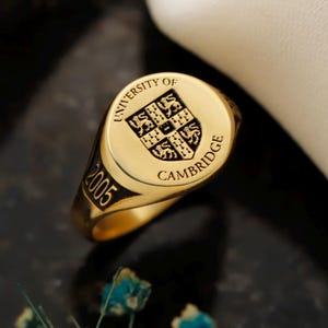 May include: A gold signet ring with the words "UNIVERSITY OF CAMBRIDGE" and the year "2005" engraved on it. The ring features a crest with a shield design.