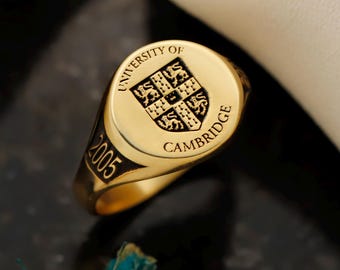 May include: A gold signet ring with the words "UNIVERSITY OF CAMBRIDGE" and the year "2005" engraved on it. The ring features a crest with a shield design.