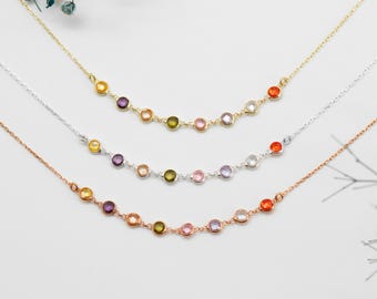 Puede incluir: Tres delicados collares con piedras preciosas de colores. Los collares son de oro, plata y oro rosa, cada uno con una serie de piedras redondas multicolores. Las piedras preciosas incluyen tonos amarillos, morados, verdes, rosas y naranjas, creando un diseño vibrante.